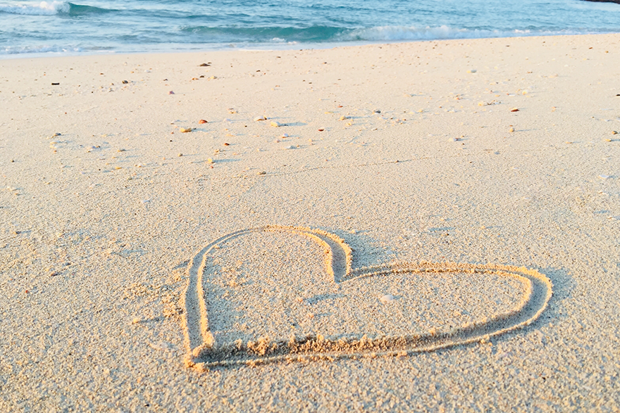 9 – Heart drawn in the sand on the beach with water in the background – unsplash